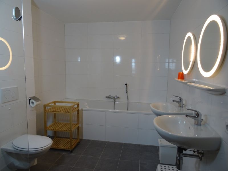 Geraeumiges Badezimmer mit Badewanne und Doppelwaschbecken in De Dors Ferienhaus Den Hoorn Texel.
