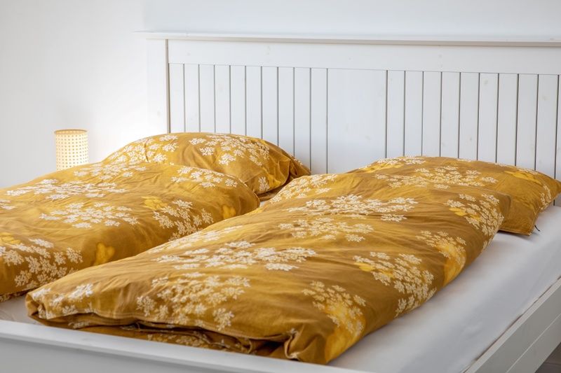 Schlafzimmer im De Zuidbunder Ferienhaus Texel mit weissen Moebeln und sonnigem Bettbezug.