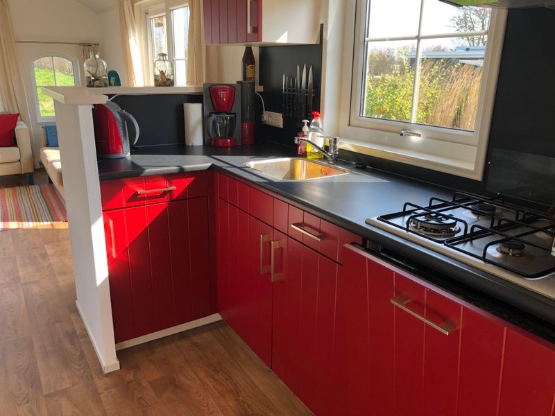 Moderne keuken in Vakantiepark De Bremakker - Akkerveld 14, vakantiehuis in De Dennen, Texel met rode kasten en uitzicht op de natuur.