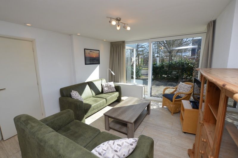 Gemuetliches Wohnzimmer des Ferienhauses de Parel 198 in De Dennen, Texel, mit bequemen gruenen Sofas und viel Tageslicht.