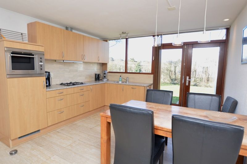 Moderne Kueche im Ferienhaus de Parel 198 in De Dennen, Texel, mit Holzschraenken und Esstisch, ideal fuer gemuetliche Mahlzeiten.