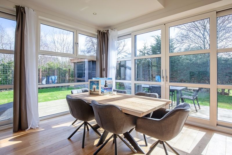 Dining area in Holiday Home De Vlinder, Texel, overlooking the green surroundings of Bungalowpark 't Hoogelandt.
