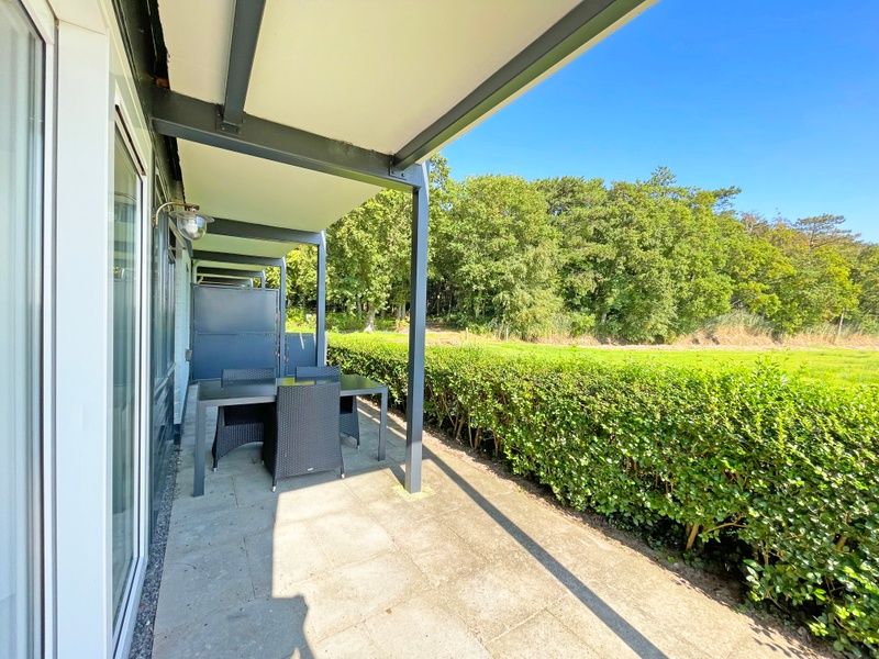 Ruim terras met tuinmeubilair in Appartement Bos en Duin 12, De Dennen, Texel, omgeven door groene natuur.