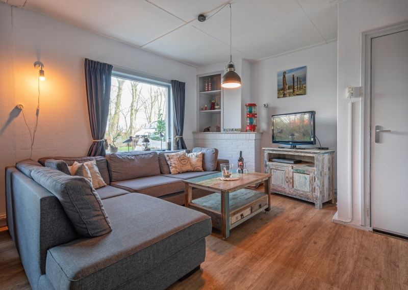 Gemuetliches Wohnzimmer des Ferienhauses Flora in De Dennen, Texel, mit bequemem Sofa und Blick auf die Natur der Watteninseln.