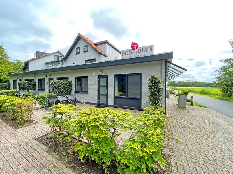 Aussenansicht des Appartements Bos en Duin 04, De Dennen, Texel, umgeben von gruener Natur und ruhiger Umgebung.