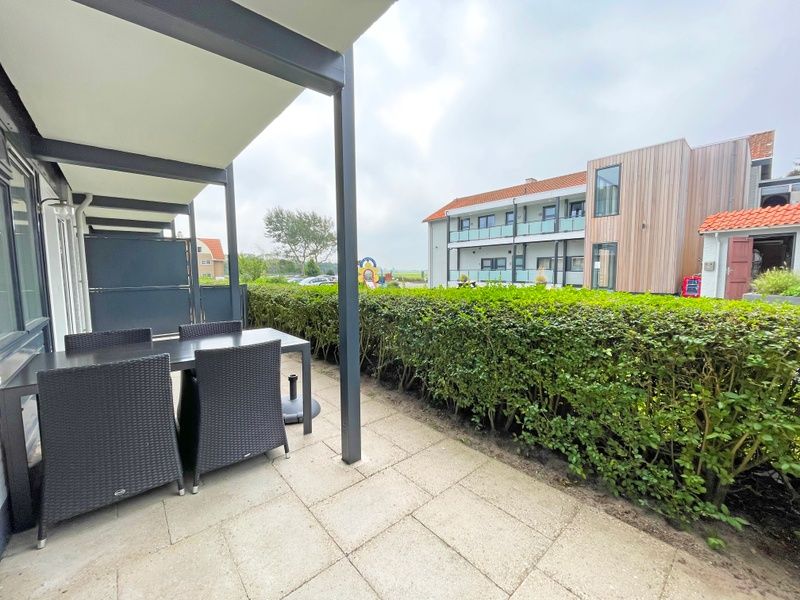 Ruim terras van Appartement Bos en Duin 10, De Dennen, Texel met tuinmeubilair en groene omgeving.