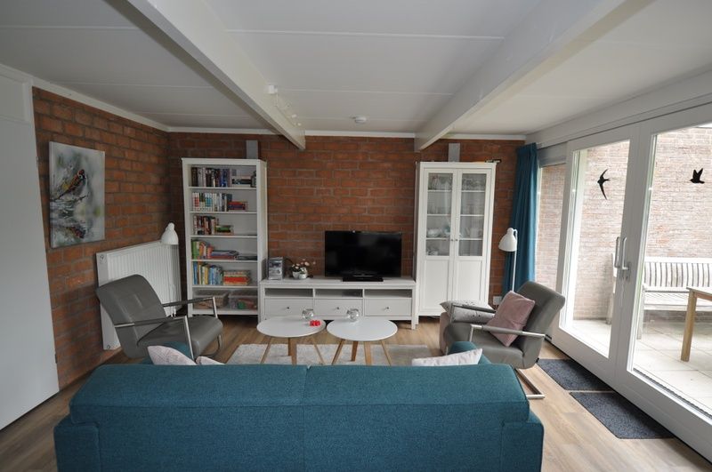 Lichte woonkamer in Bungalow Verste Coogh 62, De Dennen, Texel met comfortabele meubels en toegang tot buitenruimte.