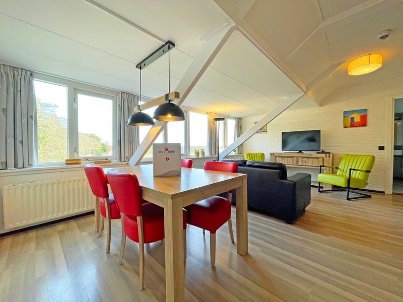 Gezellige eetruimte in Appartement Bos en Duin 36, De Dennen, Texel met houten tafel en rode stoelen.