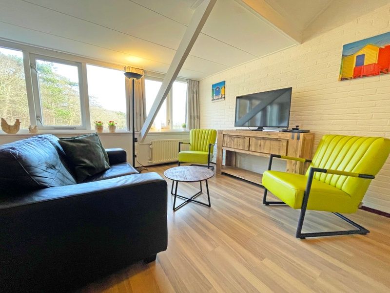 Comfortabele zithoek in Appartement Bos en Duin 36, De Dennen, Texel met groene stoelen en een flatscreen-tv.