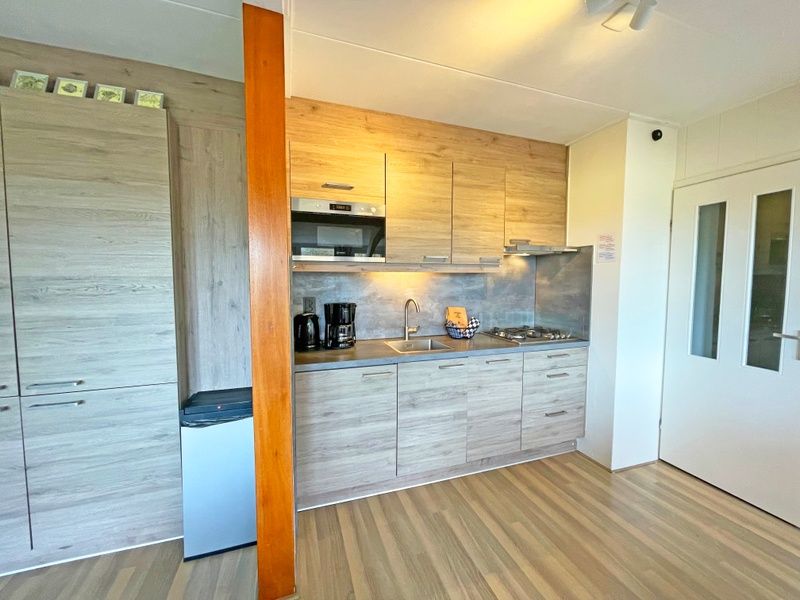 Moderne keuken in Appartement Bos en Duin 36, De Dennen, Texel met houten afwerking en inbouwapparatuur.