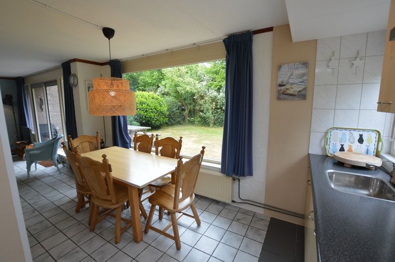 Eetkamer in Bungalow Verste Coogh 56, De Dennen, Texel, met grote ramen en zicht op de groene tuin.