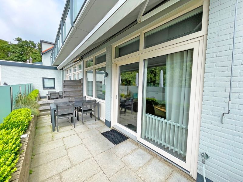 Geraeumige Terrasse des Appartements Bos en Duin 02, De Dennen, Texel mit Gartenmoebeln und gruener Umgebung.