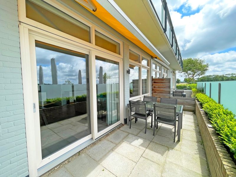 Sonnige Terrasse des Appartements Bos en Duin 03, De Dennen, Texel mit Sitzgelegenheiten und Blick auf die Natur.