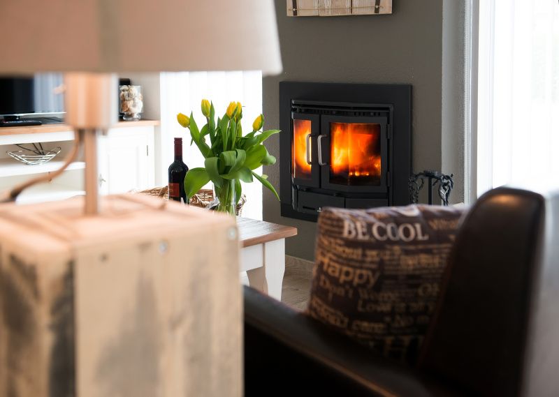 Sfeervolle open haard in de woonkamer van Gortersmient 278, Bungalowpark Gortersmient, De Dennen, Texel, met bloemen en wijn.