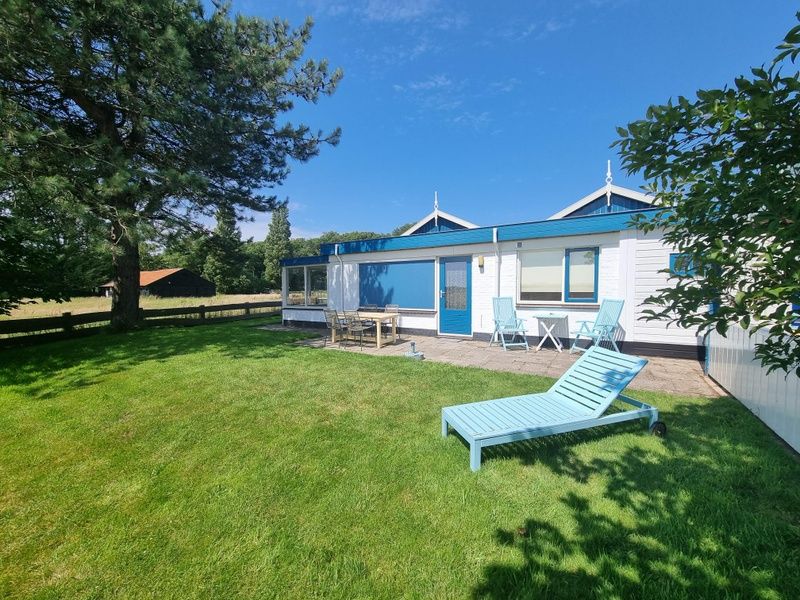 Veranda of Weidezicht vacation home in De Dennen, Texel with deck chair and garden.