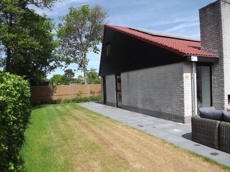 Zijaanzicht van Vakantiehuis Gortersmient 322 in De Dennen, Texel, omgeven door een groene tuin.