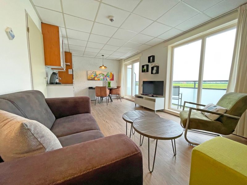 Helles Wohnzimmer des Appartements Bos en Duin 19, Texel mit gemuetlicher Sitzecke und grossen Fenstern.