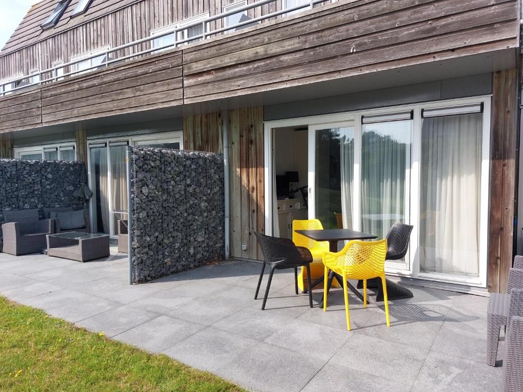 Terras van Appartement HELIOS - Amelander Kaap met ZWEMBAD in Hollum, Ameland, met kleurrijke stoelen en uitzicht op groen.
