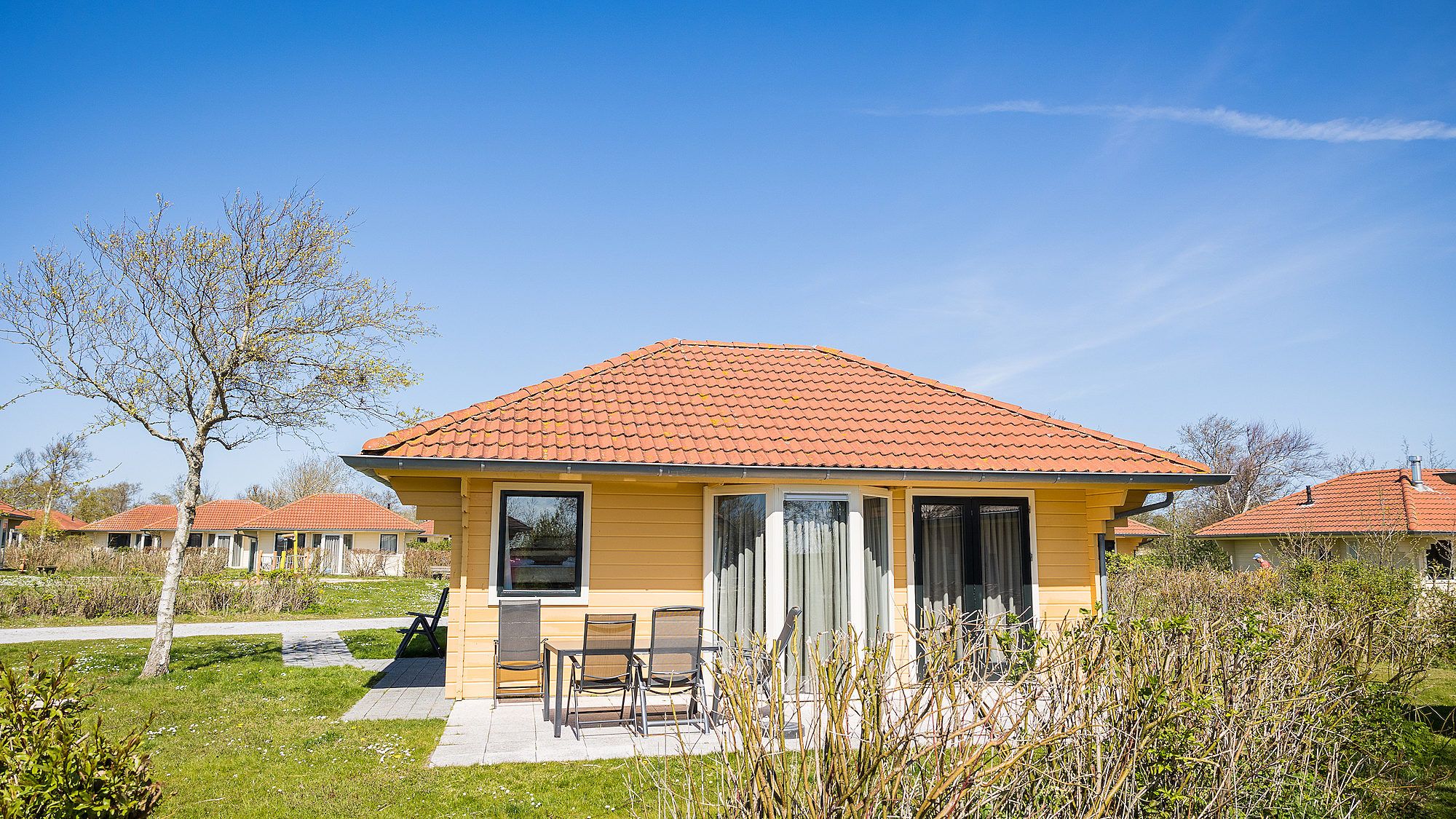 Villabungalow vakantiehuis in Oosterend, Terschelling met zonnig terras en rode dakpannen, omgeven door natuur op de Waddeneilanden.