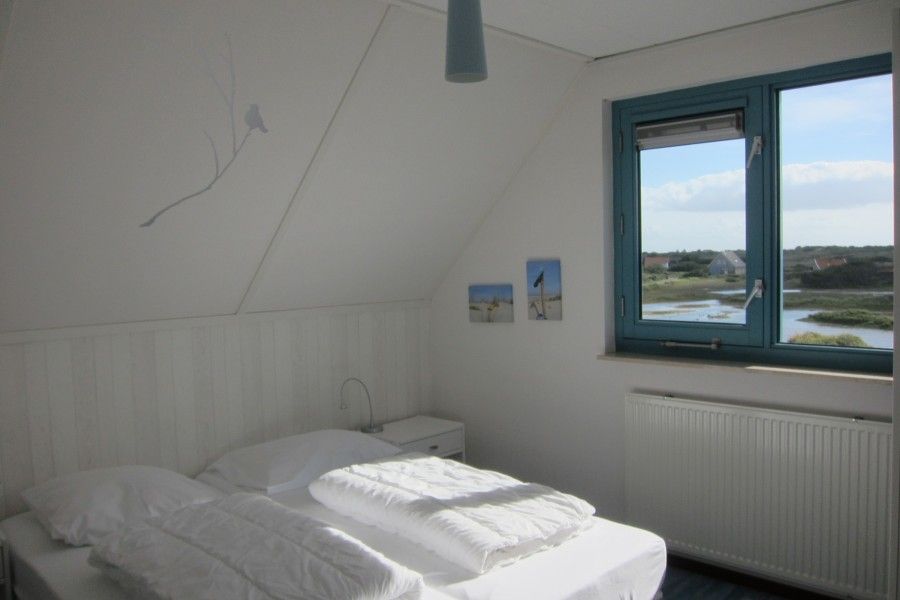 Lichte slaapkamer in Nij Jit vakantiehuis, Midsland aan Zee Terschelling, met uitzicht op water en duinen.