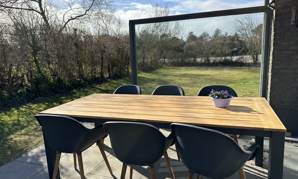 Houten eettafel op het terras van Zeevonk vakantiehuis in Ballum, Ameland, met uitzicht op de groene omgeving.