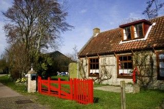 Vacation home Suzan in Ballum, Ameland with charming facade and red gate, surrounded by nature on the Wadden Islands.