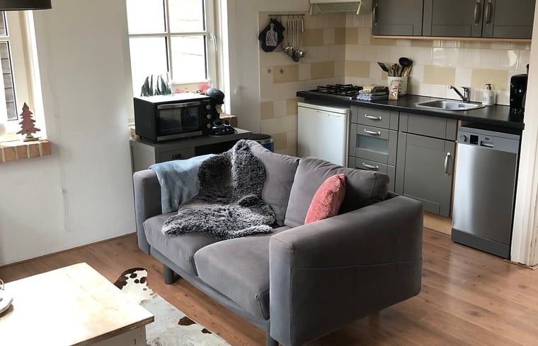 Comfortabele woonkamer in Vakantiehuisje in Buren Ameland met knusse bank en open keuken, ideaal voor ontspanning.