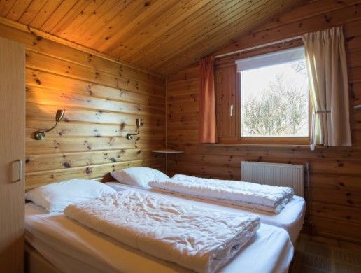 Schlafzimmer im FINSE BUNGALOW 4, Hollum, Ameland, mit gemuetlicher Holzeinrichtung und Blick auf die Natur.
