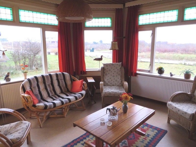 Gemuetliche Sitzecke im Ferienhaus Zeerust auf Schiermonnikoog, Watteninseln, mit Blick auf die Natur und bequemen Rattanmoebeln.