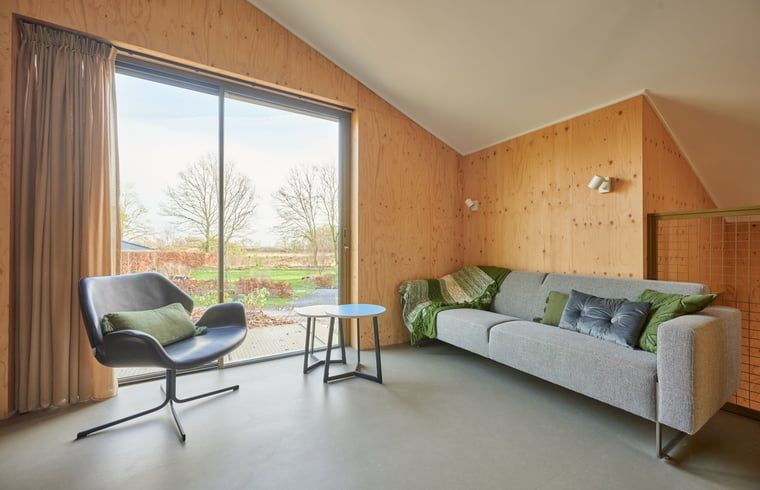 Stijlvolle zithoek in Vakantiehuisje in Spier, met grote ramen en uitzicht op de tuin.