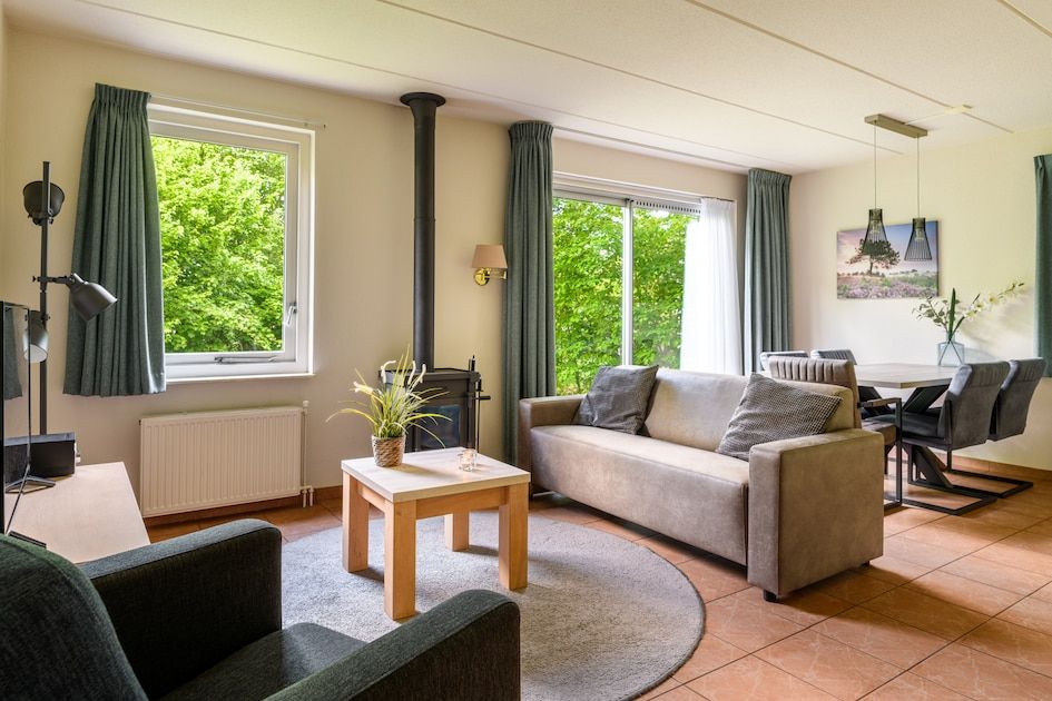Gemuetliches Wohnzimmer des Comfort Plus 5 Bungalows in Hoogersmilde, Zentral-Drenthe, mit Blick auf die gruene Natur.
