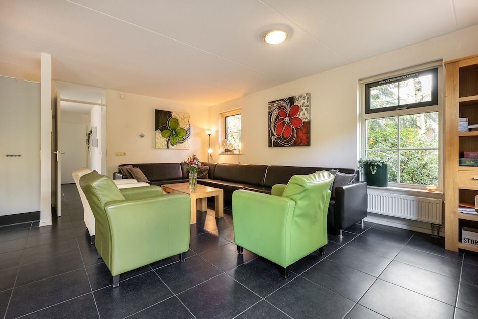 Gemuetliches Wohnzimmer der Zandduin Villa mit Sauna 10 in Hooghalen, Zentral-Drenthe, mit bequemen Sitzgelegenheiten und Blick auf die Natur.