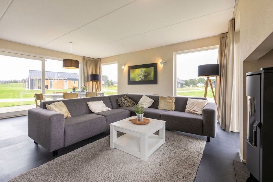 Spacious living room in bungalow Drentsche Aa 6, Tynaarlo, North Drenthe, with comfortable sofa and view of green surroundings.