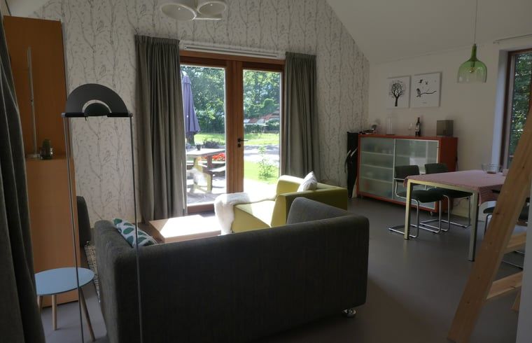 Gezellige woonkamer van Huisje in Bunne, vakantiehuis in Noord Drenthe, met uitzicht op groene tuin door openslaande deuren.