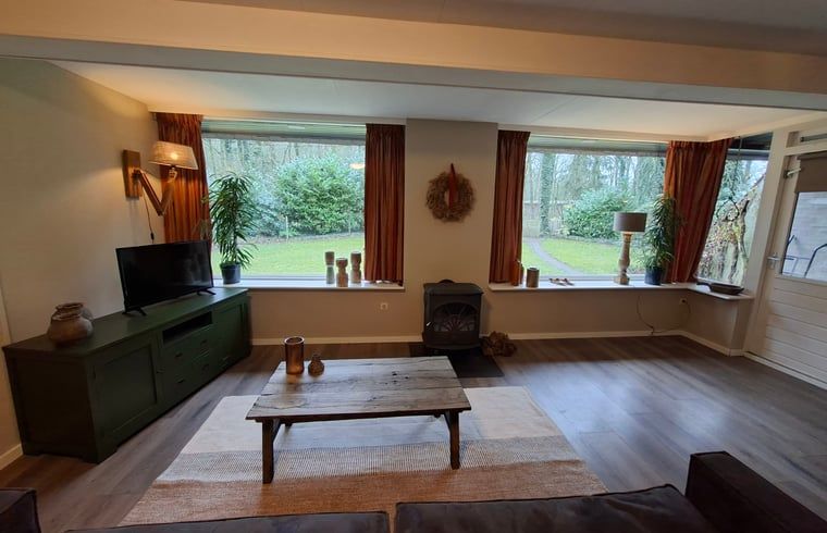 Gemuetliches Wohnzimmer des Ferienhauses in Schoonoord mit Blick auf den gruenen Garten, gelegen in Suedost-Drenthe, Drenthe.