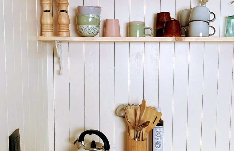 Gemuetliche Kuechenecke in Cottage in Zuidwolde, Ferienhaus in Zuidwolde, Drenthe mit Wandregalen aus Holz und bunten Tassen.