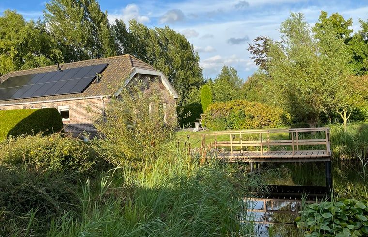 Huisje in Nieuweroord, vakantiehuis in Zuidwest Drenthe met uitzicht op een serene tuin en houten brug.