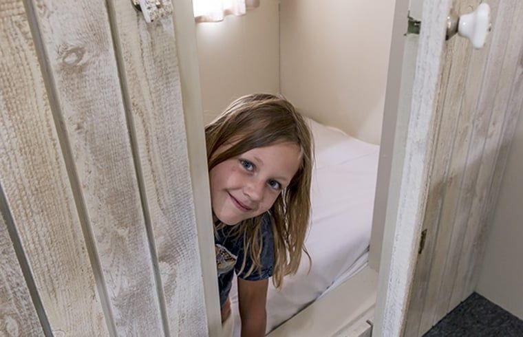 Kind glimlacht in knusse slaapkamer van Huisje in Wapserveen, Zuidwest Drenthe, Drenthe.