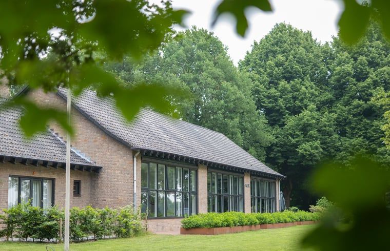 Buitenkant van Vakantiehuisje in Dwingeloo, Drenthe, omgeven door groene bomen en gras.