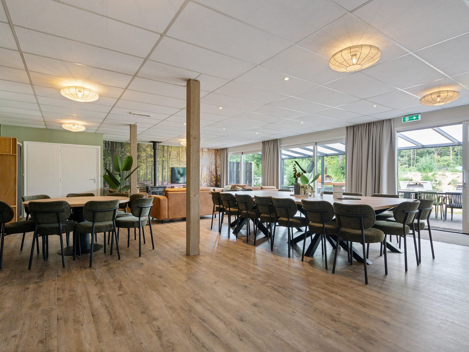 Ruime binnenruimte van Groepsaccommodatie de Komeet in Dwingeloo, Drenthe, met grote tafels en uitzicht op de groene omgeving.