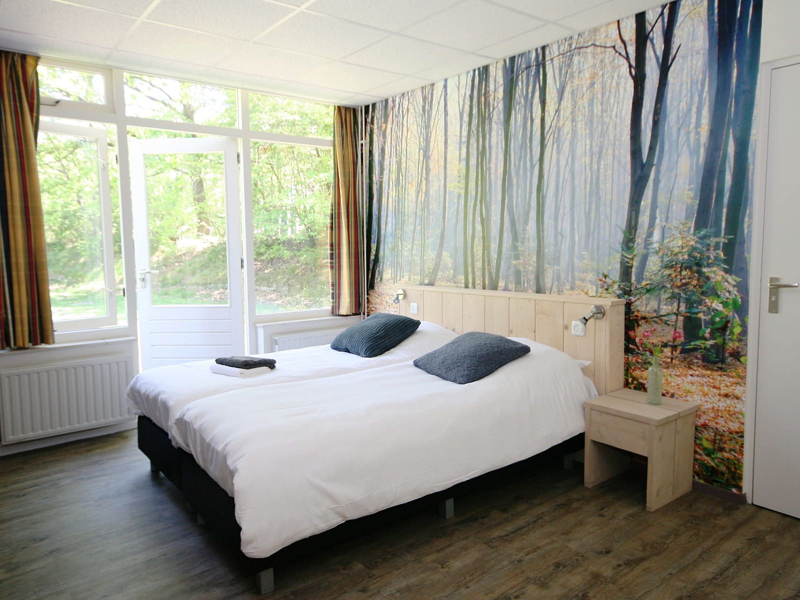 Sfeervolle slaapkamer in Groepsaccommodatie de Komeet, Dwingeloo, Zuidwest Drenthe, met bosrijk behang en uitzicht op de natuur.