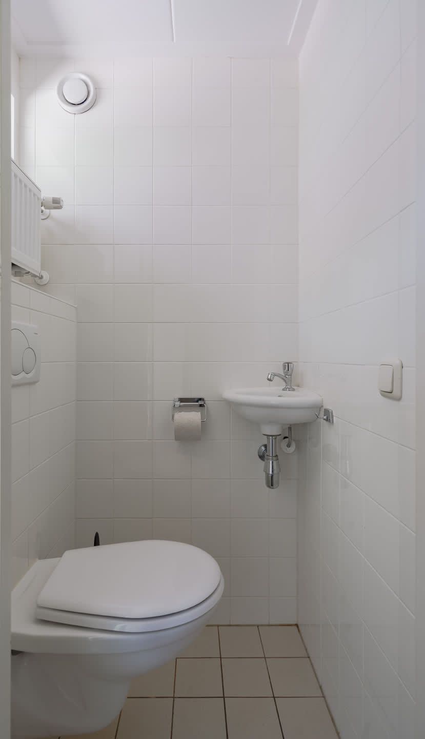 Moderne badkamer in Bungalow Mars, een vakantiehuis in Dwingeloo, Zuidwest Drenthe, met strakke witte tegels en een compacte wastafel.