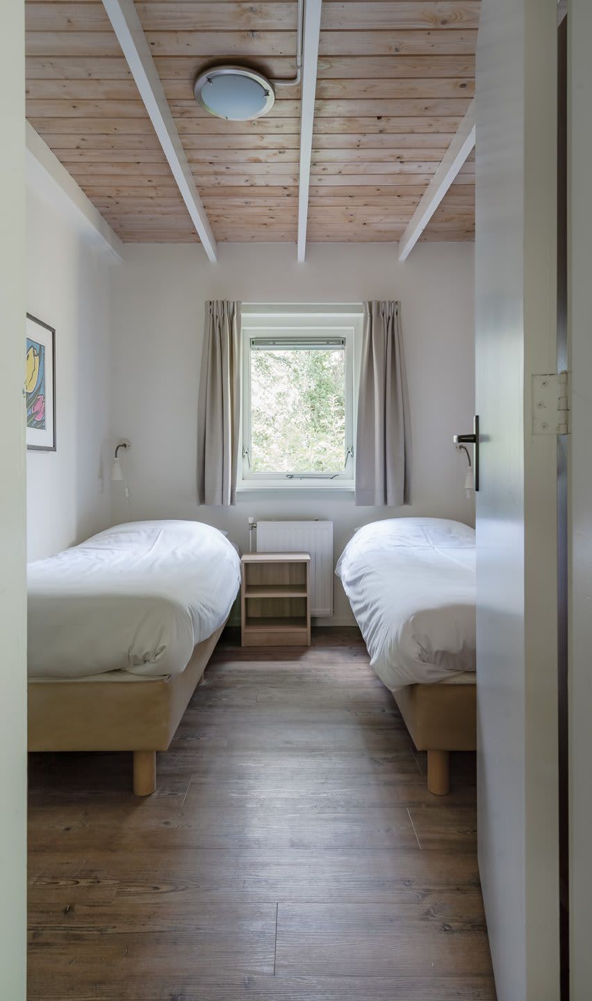 Gezellige slaapkamer in Bungalow Saturnus, Dwingeloo, met twee eenpersoonsbedden en uitzicht op de groene omgeving van Zuidwest Drenthe.