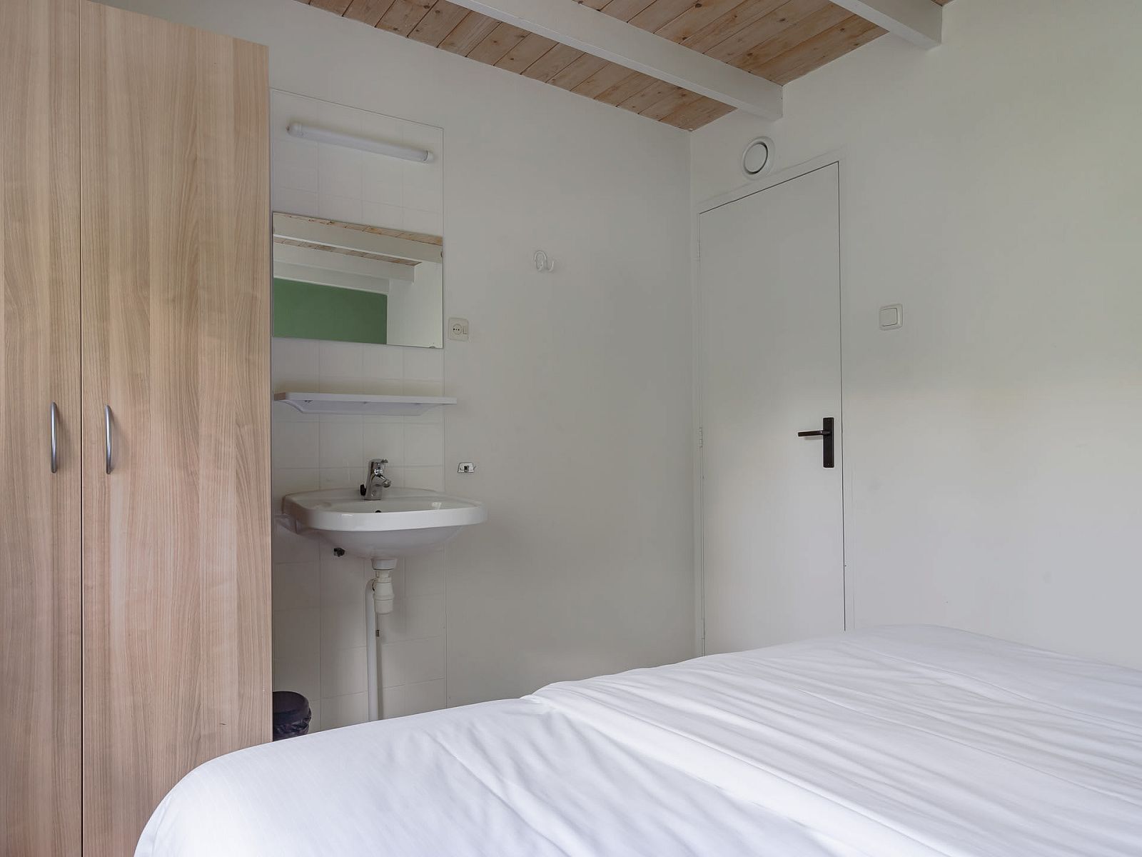 Slaapkamer in Bungalow Saturnus, een vakantiehuis in Dwingeloo, Zuidwest Drenthe, met een comfortabel bed en een praktische wastafel.