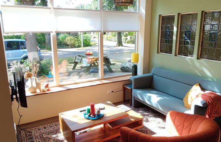 Charmante Terrasse am Ferienhaus in Dwingeloo, Suedwest-Drenthe, mit bequemen Stuehlen und Sonnenschirm.