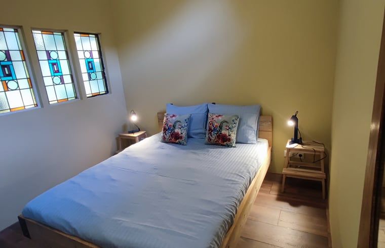 Gemuetliches Schlafzimmer im Ferienhaus in Dwingeloo, Suedwest-Drenthe, mit bunten Kissen und stimmungsvollen Glasmalereien.