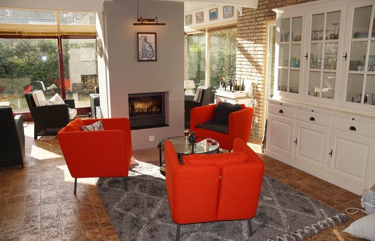 Zonovergoten woonkamer in Vakantiehuis in Zorgvlied, Zuidwest Drenthe, met comfortabele rode stoelen.