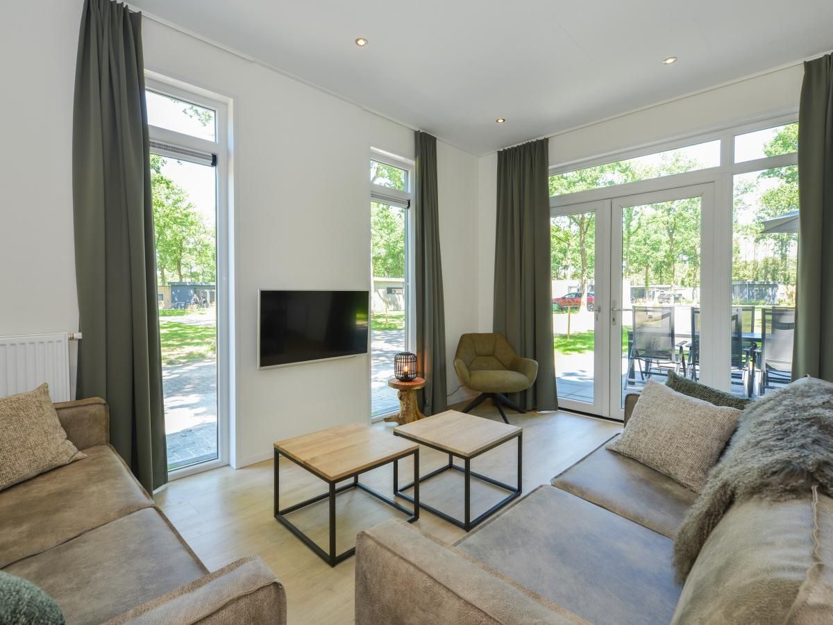 Gezellige woonkamer van chalet Onderduikershol in Zorgvlied, Zuidwest Drenthe met uitzicht op groene natuur en comfortabele zithoek.