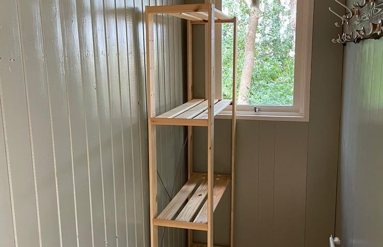 Binnenruimte van Huisje in Wateren, vakantiehuis in Zuidwest Drenthe, met houten opbergrek en uitzicht op groene natuur door het raam.