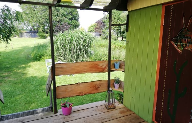Uitzicht vanaf de veranda van vakantiehuis in Elim, Drenthe, met groene tuin en zonlicht.